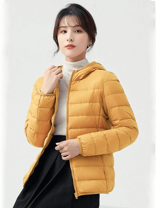 Woman wearing a stylish yellow down jacket with hood, perfect for outdoor activities. Lightweight, warm, and waterproof design.